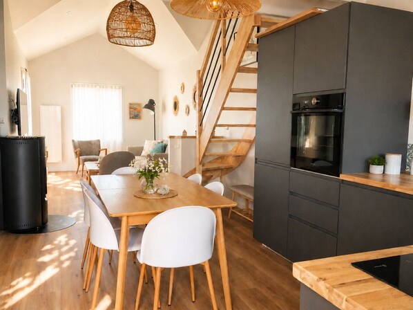 A modern kitchen with a black refrigerator, wooden dining table, white chairs, and a wooden staircase.