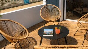 Ein Balkon mit Korbstühlen, einem Tisch mit einem Buch und einem Getränk, und Blick auf den Strand.