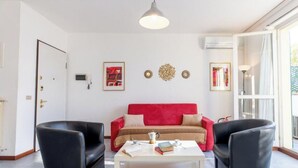 A living room with a red sofa, two black armchairs, a white coffee table, and a large window.