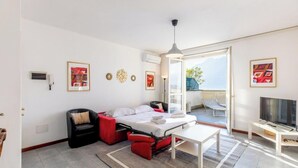 A compact hotel room with a bed, a seating area, a television, and a view of the outdoors.