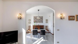 A dining area with a table and chairs, a television, and wall-mounted lighting fixtures.