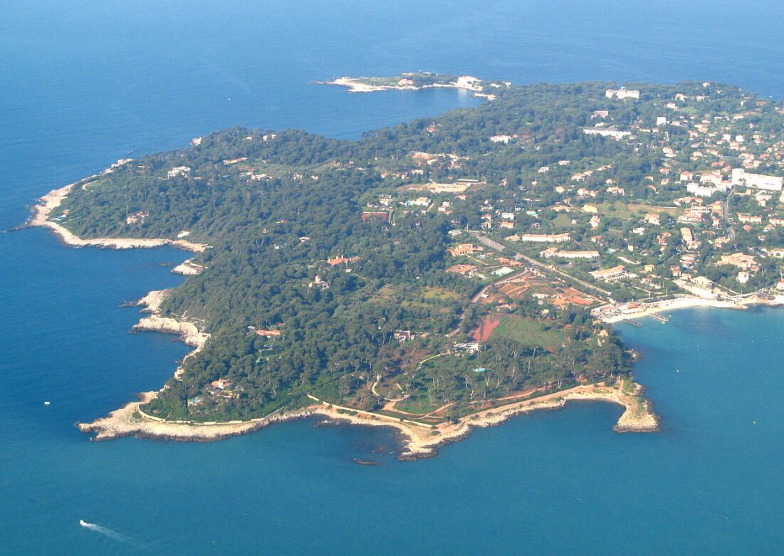An aerial view of a coastal island with dense vegetation, a mix of residential and commercial buildings, and a clear coastline.