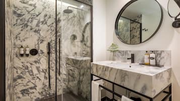 A modern bathroom with a glass-enclosed shower, marble countertops, and a round mirror.