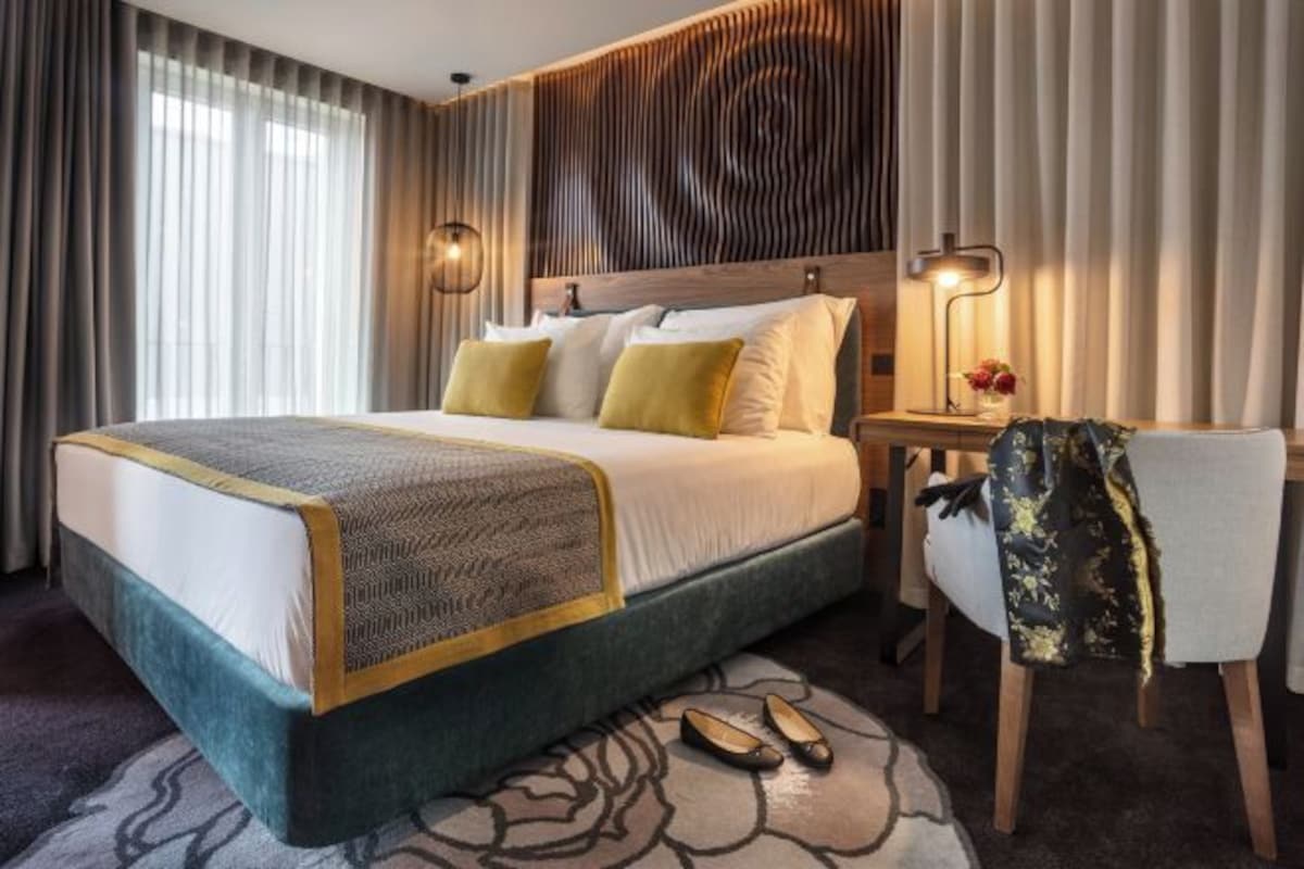 Une chambre d’hôtel avec un grand lit, une table de chevet avec une lampe, une chaise et un tapis à motifs.