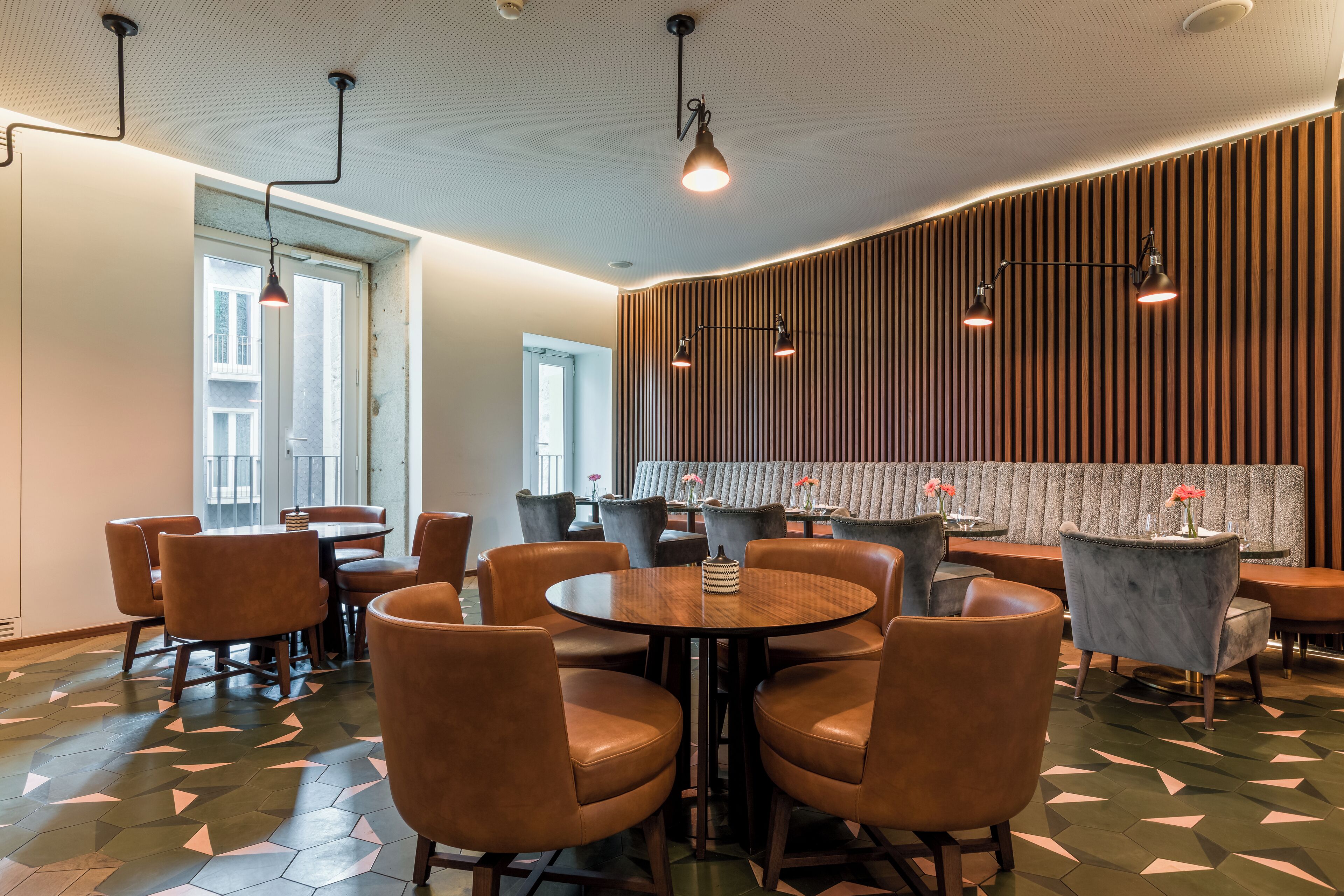 Un comedor moderno con mesas redondas y sillas de cuero, paneles de madera en la pared e iluminación colgante.