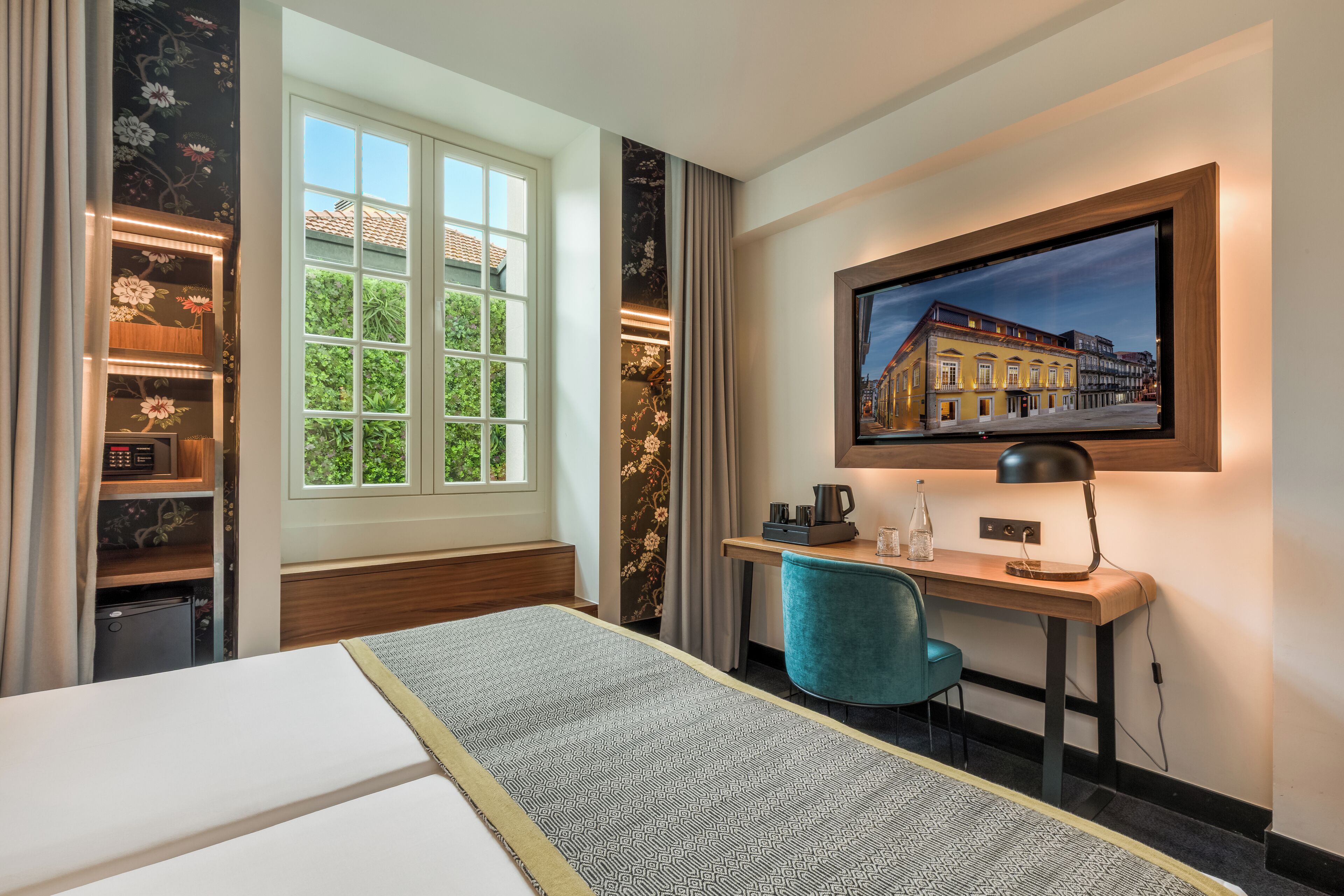Una habitación de hotel con cama, escritorio con silla, televisión y ventana con vista a edificios.
