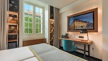 Una habitación de hotel con cama, escritorio con silla, televisión y ventana con vista a edificios.