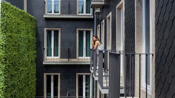 Un edifici de diverses plantes amb balcons, una tanca de fulles verdes i una barana metàl·lica.