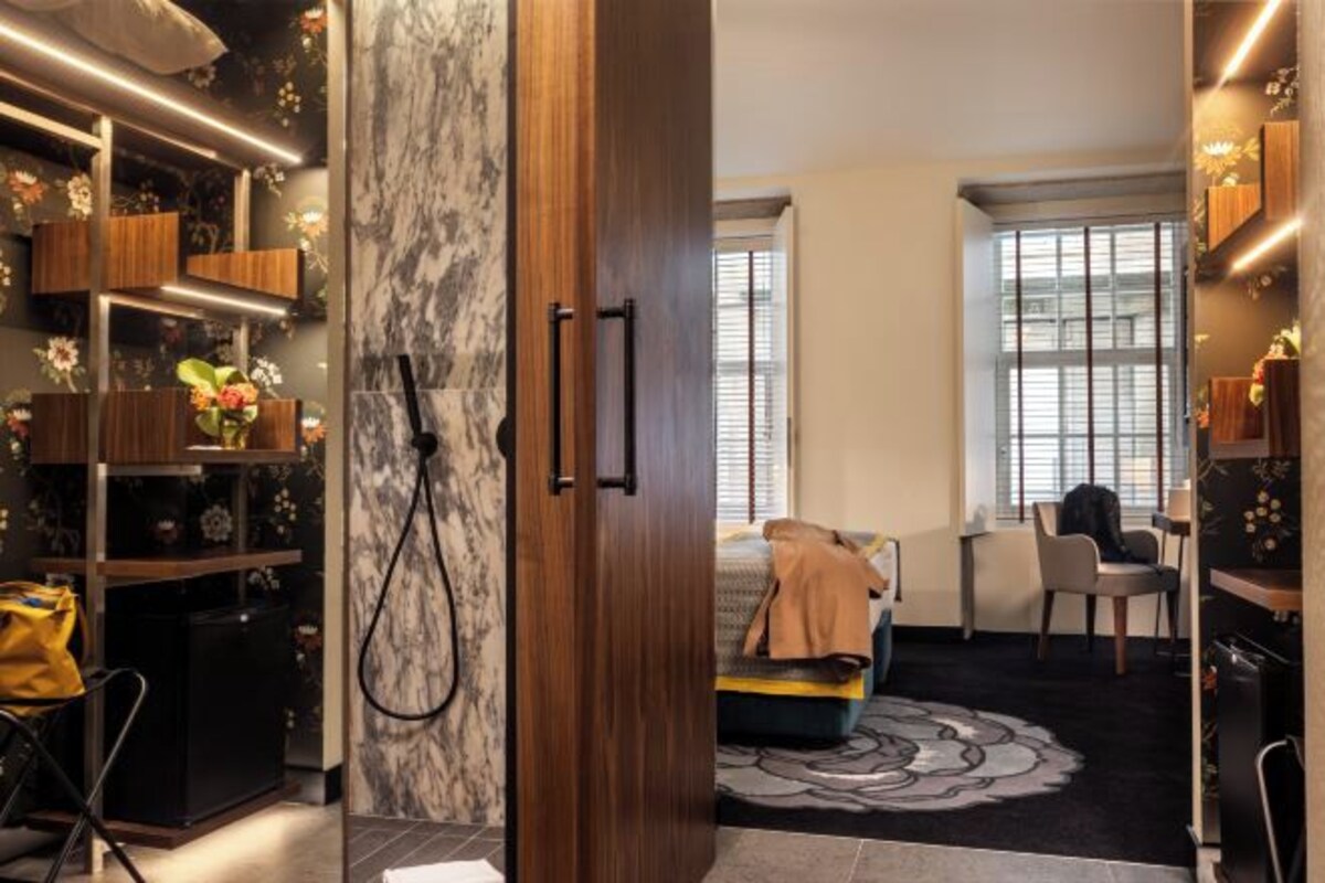 Une chambre à coucher moderne avec un lit, un bureau et une chaise. On y trouve une armoire en bois et une étagère ornée de fleurs.