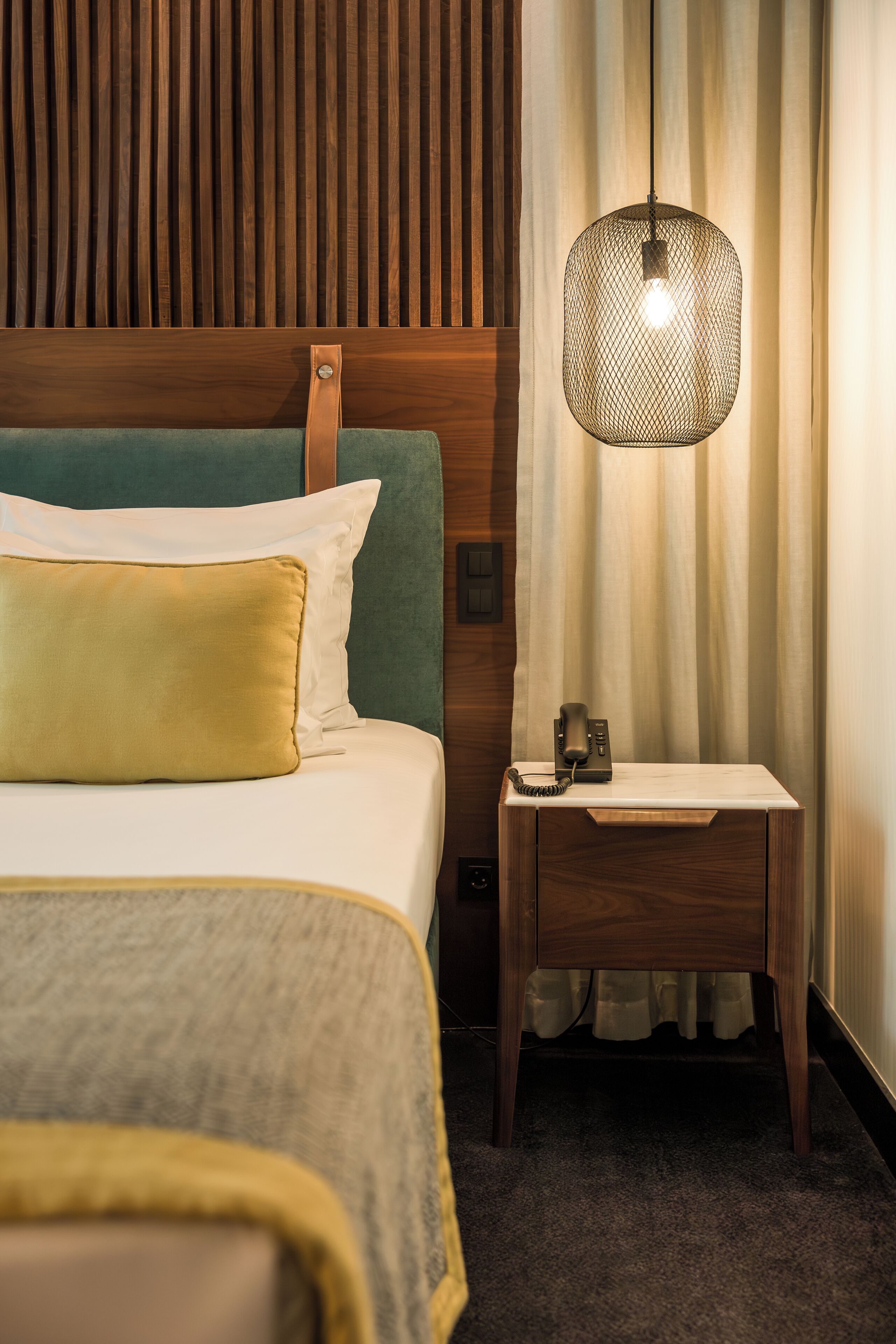 A hotel room with a bed, a nightstand, a telephone, and a hanging light fixture.