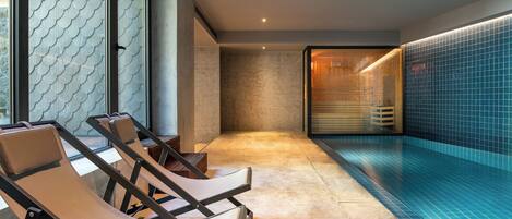 Un área de piscina interior moderna con sillones de descanso y una pared de azulejos azules.