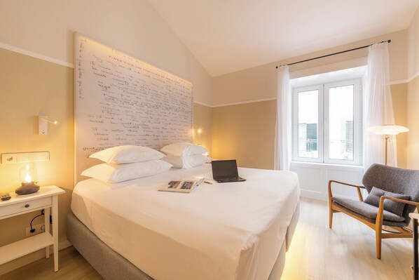 A hotel room with a large bed, a laptop, a chair, and a window with curtains.