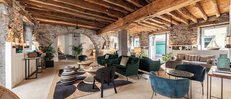 Un'ampia zona giorno con un'architrave rustica in pietra, travi in legno e arredamento moderno.