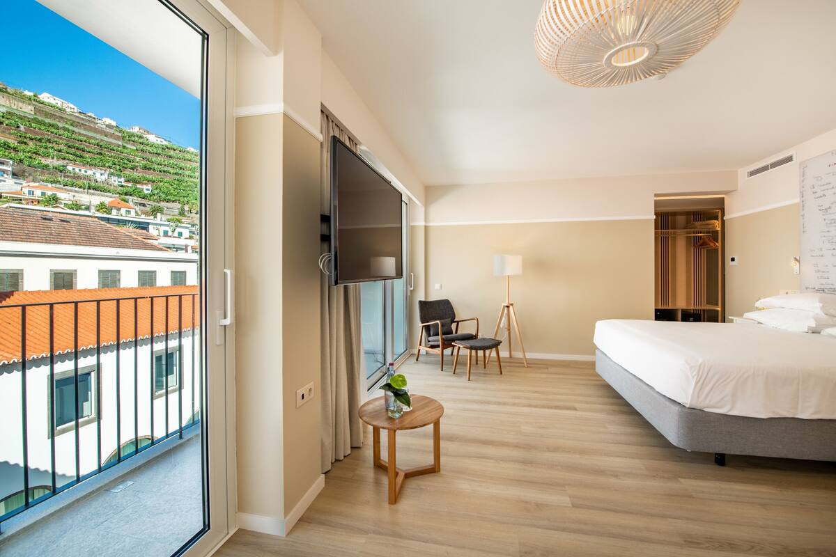 Ein Hotelzimmer mit Balkon, einem Bett, einem Schreibtisch, einem Stuhl und einem Kleiderschrank.