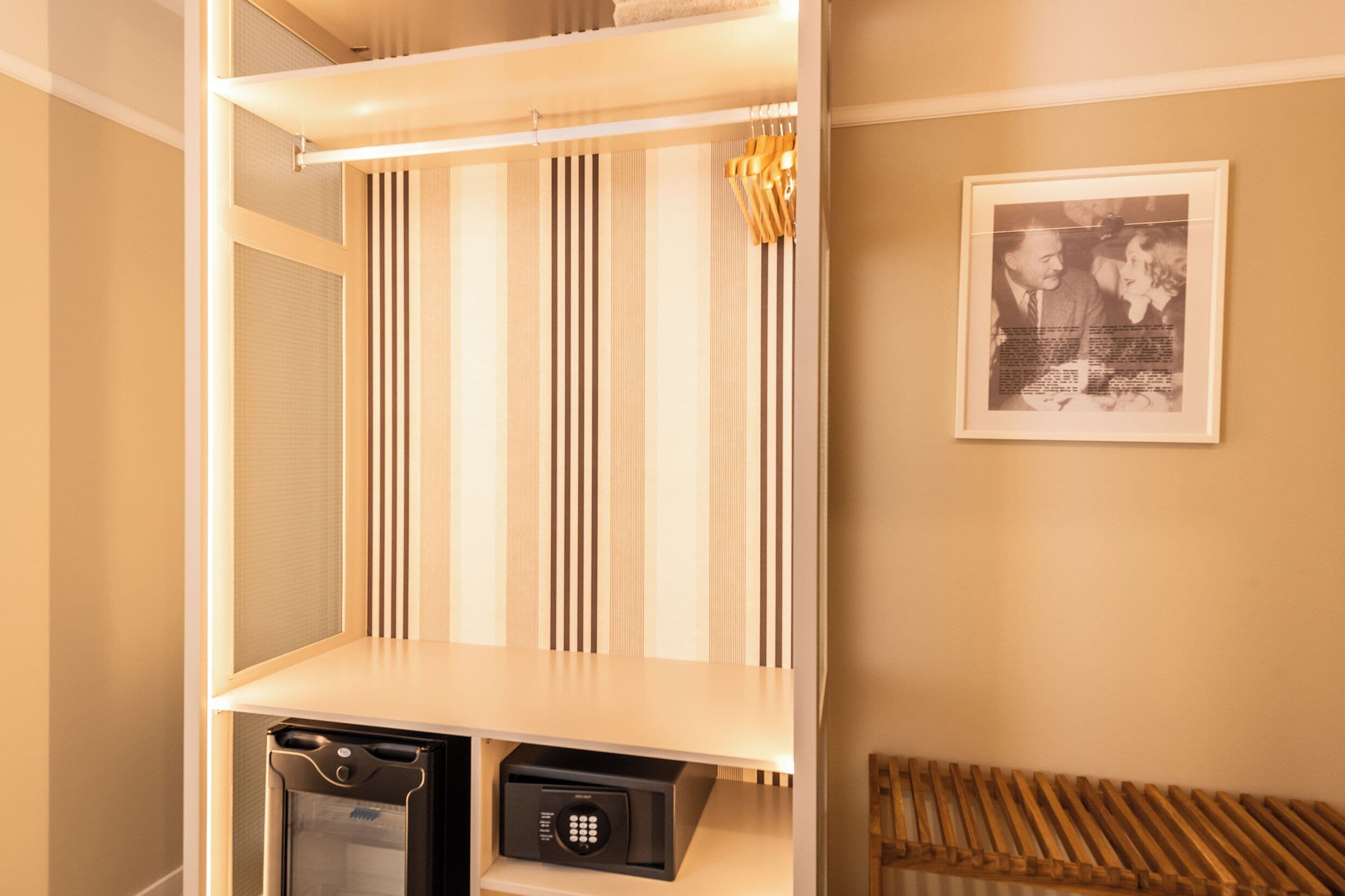 Habitación con armario de espejo, una fotografía en el marco en la pared y una pequeña caja fuerte en el suelo.