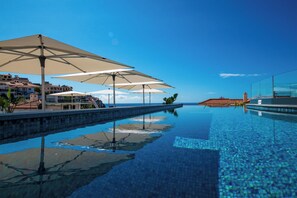 A swimming pool with clear blue water, surrounded by lounge chairs and umbrellas, and buildings in the background.