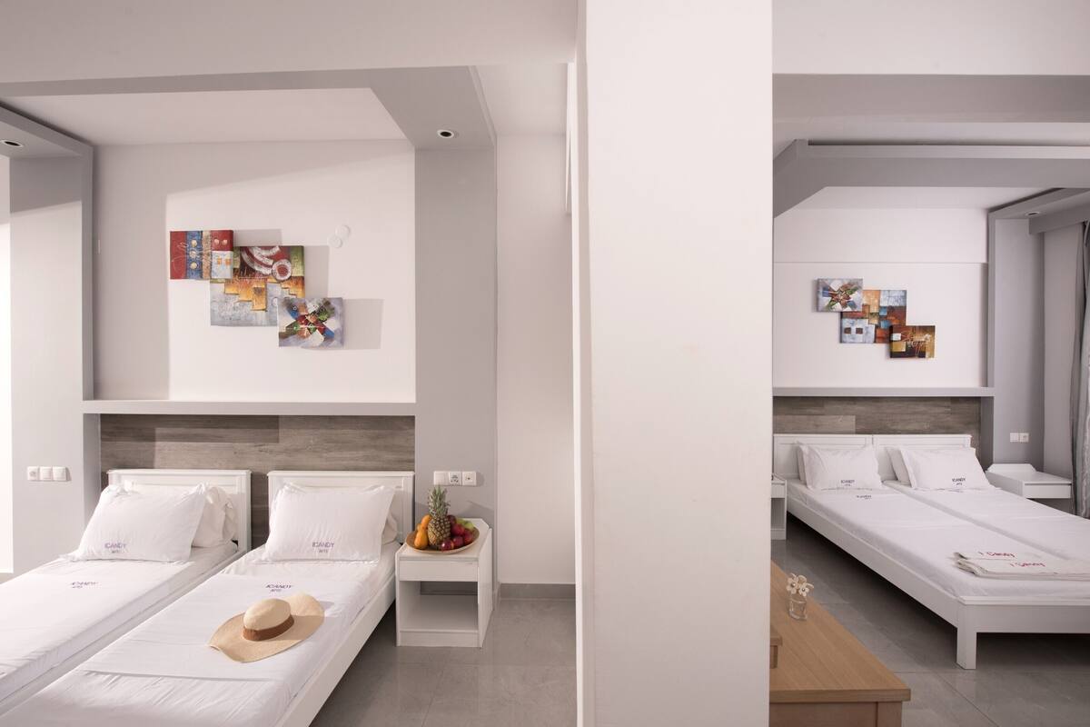 A modern hotel room with two single beds, a small bedside table with a fruit bowl, and a wall-mounted artwork.