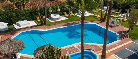 A swimming pool with sun loungers and palm trees.