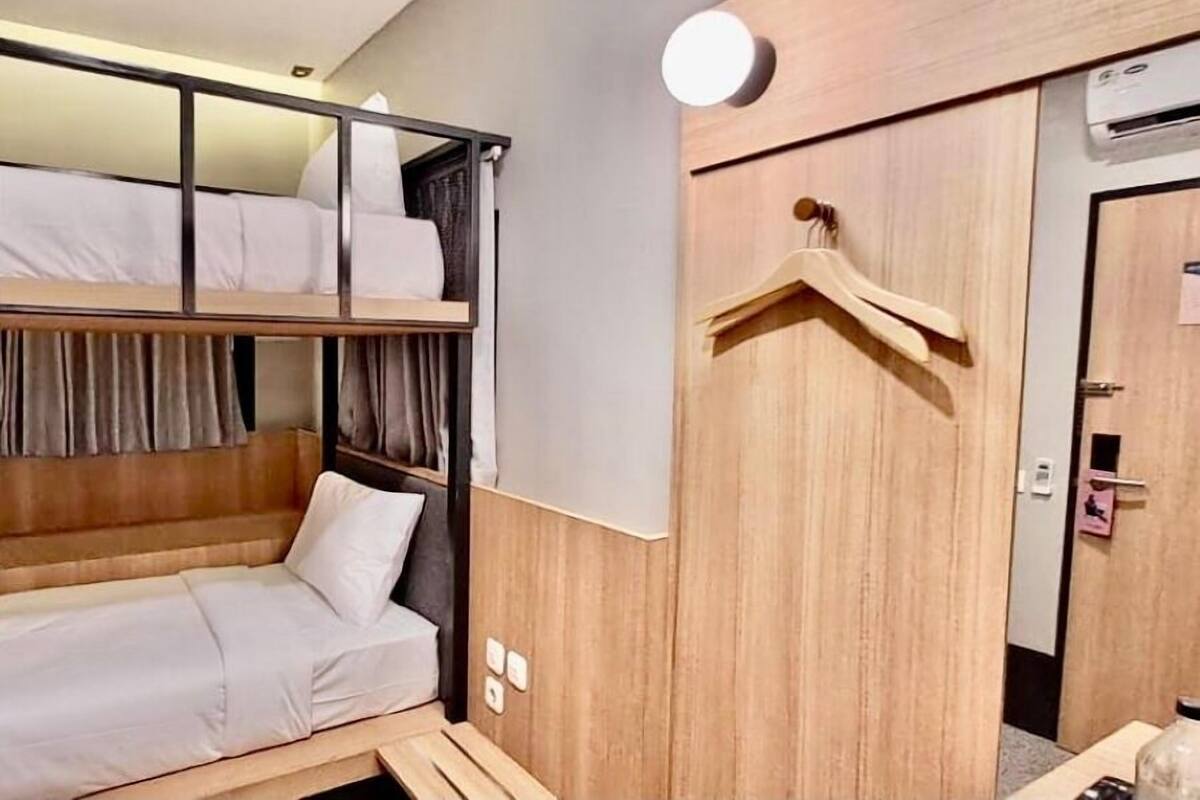 A hotel room with a bunk bed, a wooden wardrobe, a hanging clothes rack, and an air conditioning unit.
