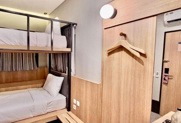 Une chambre d’hôtel équipée d’un lit superposé, d’une armoire en bois, d’un portant à vêtements et d’un appareil de climatisation.