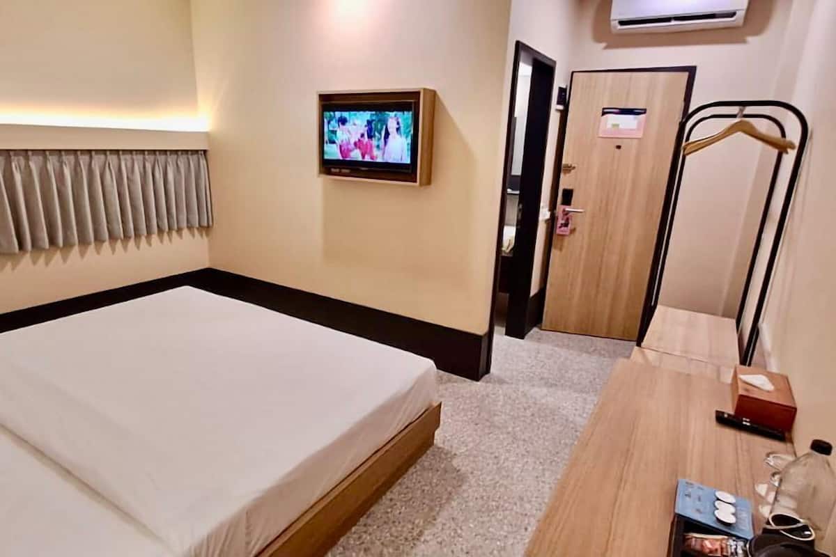 A hotel room with a bed, a TV mounted on the wall, a wooden desk with a chair, and a door with a coat rack.