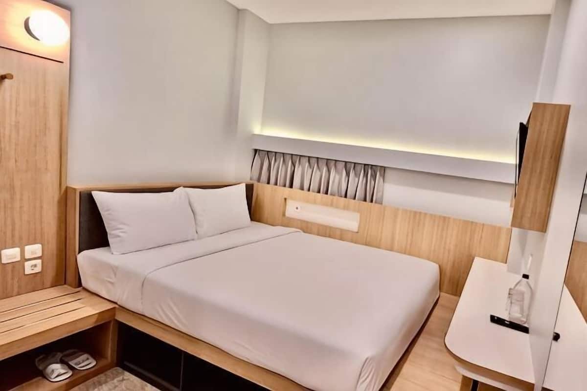 A modern hotel room with a bed, bedside table, and a small desk area.