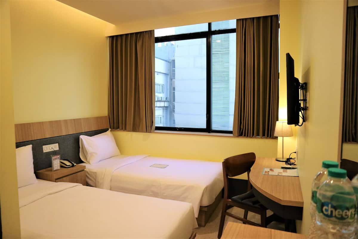 A hotel room with two beds, a desk, a chair, a TV, and a window with curtains.