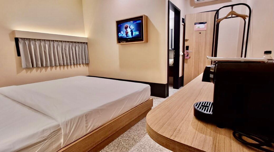 Habitación de hotel con cama, televisión montada en la pared, escritorio de madera y masajeador de pies.