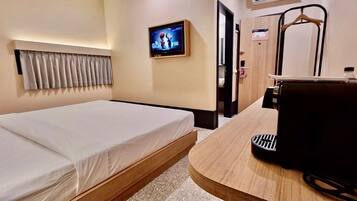 A hotel room with a bed, a TV mounted on the wall, a wooden desk, and a foot massager.