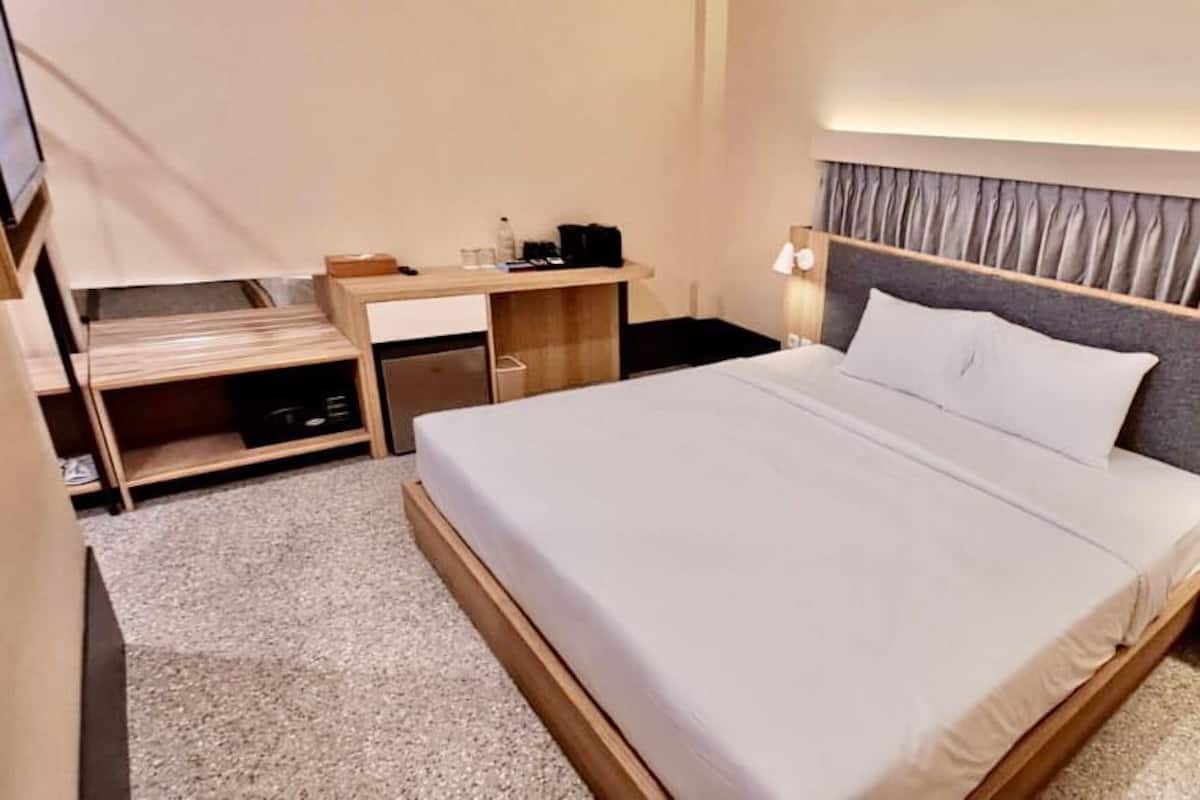 A hotel room with a large bed, a wooden desk, a chair, a nightstand, and a lamp.