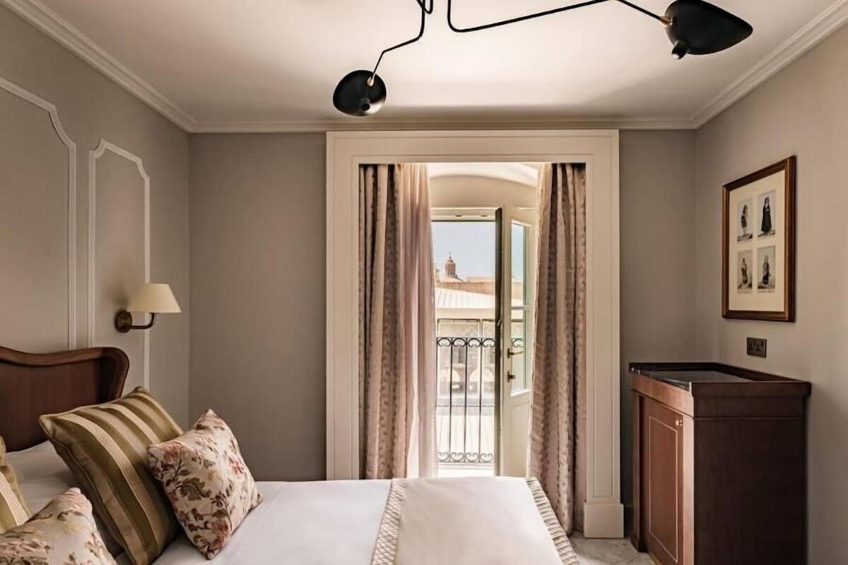 Habitación de hotel con cama, escritorio, lámpara y vista a través de una puerta.