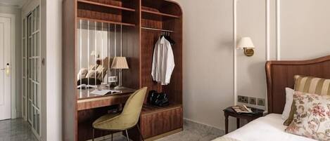 Habitación de hotel con un escritorio de madera, una silla, una cama con almohadas estampadas, una mesita de noche, una lámpara y un armario.