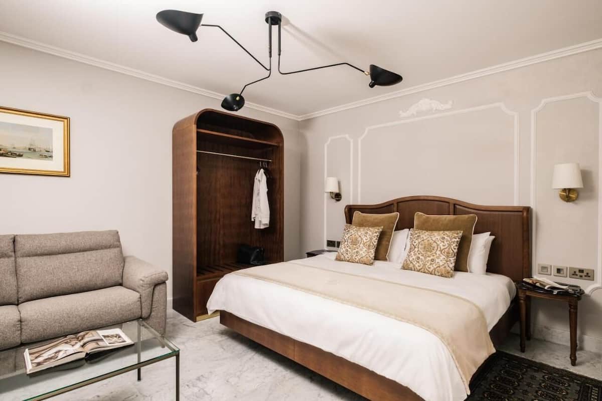 Una habitación de hotel con una cama, un sofá, un armario de madera, una mesa de centro de vidrio y una lámpara de pared.