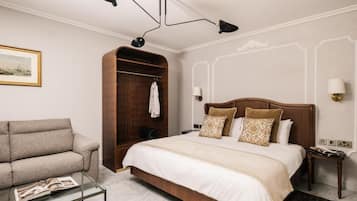 A hotel room with a bed, a sofa, a wooden wardrobe, a glass coffee table, and a wall-mounted lamp.