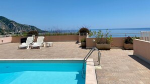 En pool på taket med solstolar och utsikt över havet.