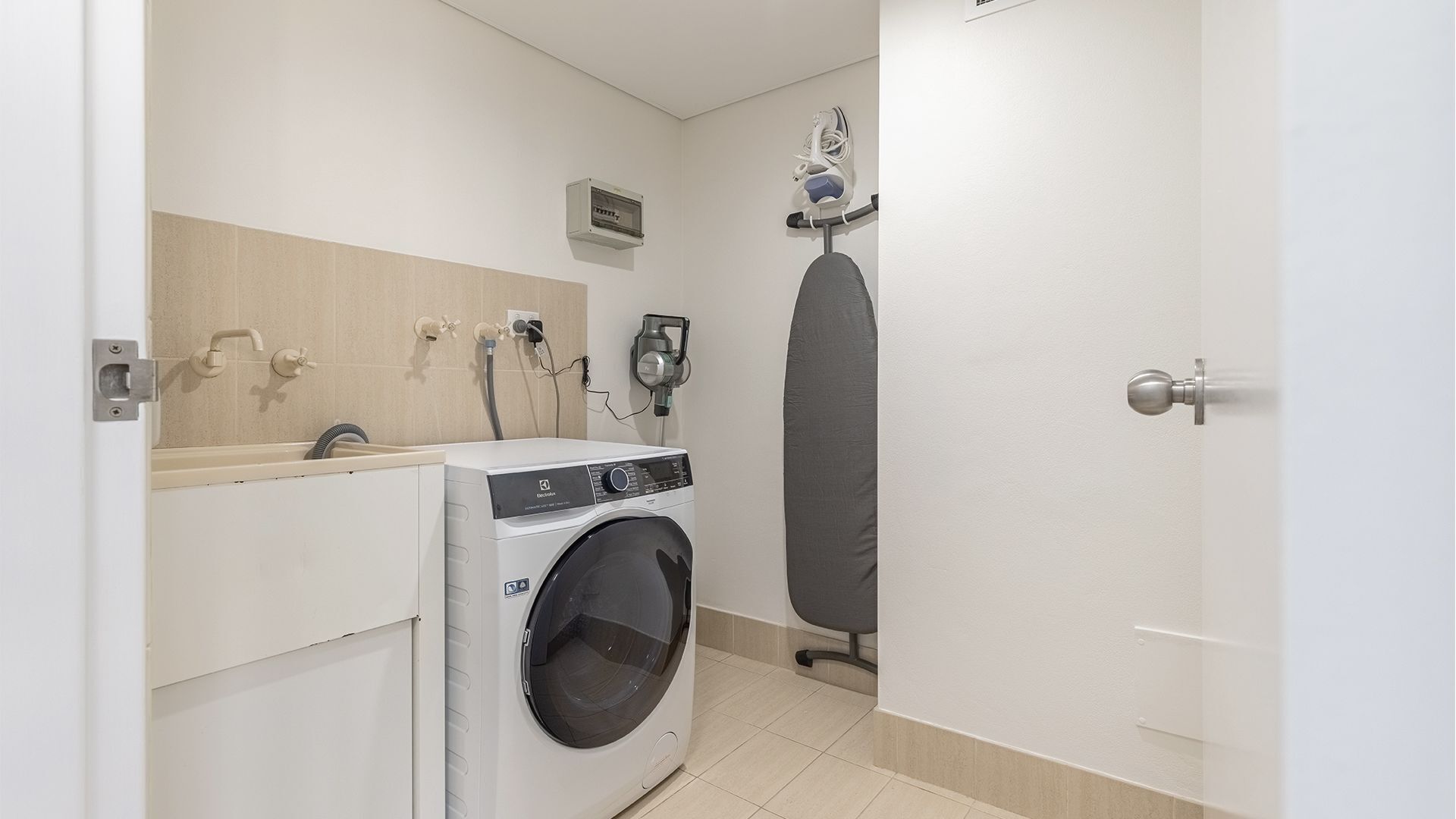 Een kleine wasruimte met een voorlader wasmachine, een wandplank voor het strijken en een klein stopcontact.