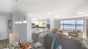A modern living room with a dining area, a kitchen, and a large window overlooking a beach. - Pelican Sands 2 , 83 Soldiers Point Road - fantastic waterfront unit with pool and air conditioning (Soldiers Point)