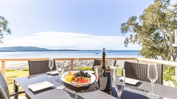 A table set for two with a view of the sea, a bottle of champagne, and a plate of food. - Pelican Sands 2 , 83 Soldiers Point Road - fantastic waterfront unit with pool and air conditioning (Soldiers Point)
