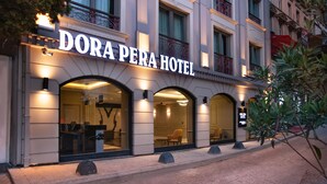 El exterior del Hotel Dora Perla con señalización iluminada, grandes ventanas arqueadas y un balcón con barandillas ornamentales.