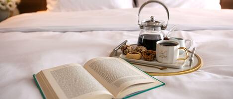 A neatly made bed with a book, a teapot, and cookies on a tray.