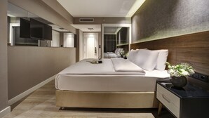 Una habitación de hotel moderna con una cama grande, un televisor de pantalla plana, una mesita de noche con un jarrón de flores y un espejo grande en la pared.