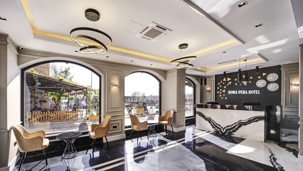 Un moderno vestíbulo de hotel con una recepción, un área de descanso y grandes ventanales que ofrecen vistas a la ciudad.