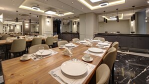 Comedor de hotel con varias mesas dispuestas para el servicio, iluminación moderna y suelo de mármol.