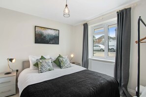 A bedroom with a bed, a bedside table with a lamp, a window with curtains, and a painting on the wall. - Hawthorn - Oxford (Oxford)