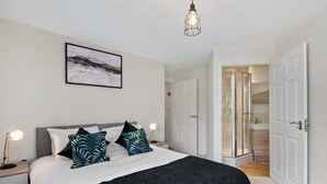 A bedroom with a bed, bedside lamps, a framed picture on the wall, and a door leading to a bathroom.
