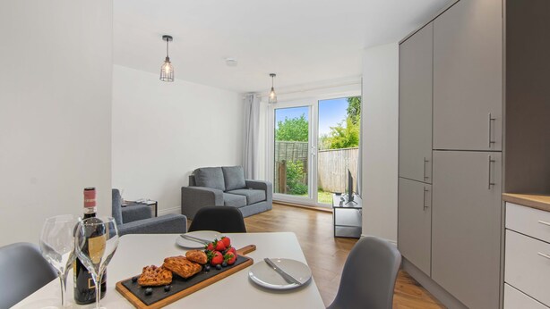 A modern kitchen with a dining table set for two, a bottle of wine, and a fruit platter.