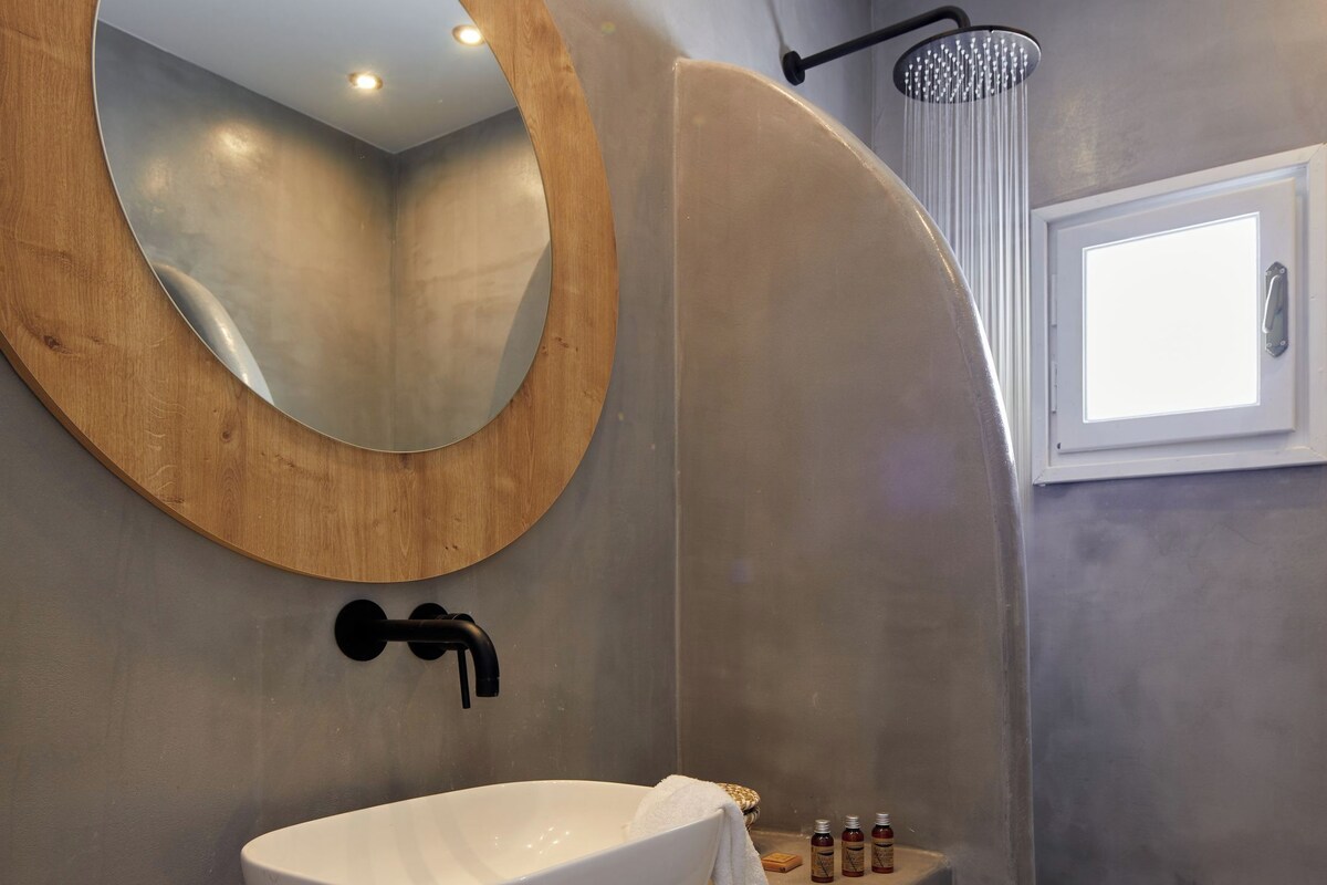A modern bathroom with a round mirror, a white sink, a towel rack, and a shower area.
