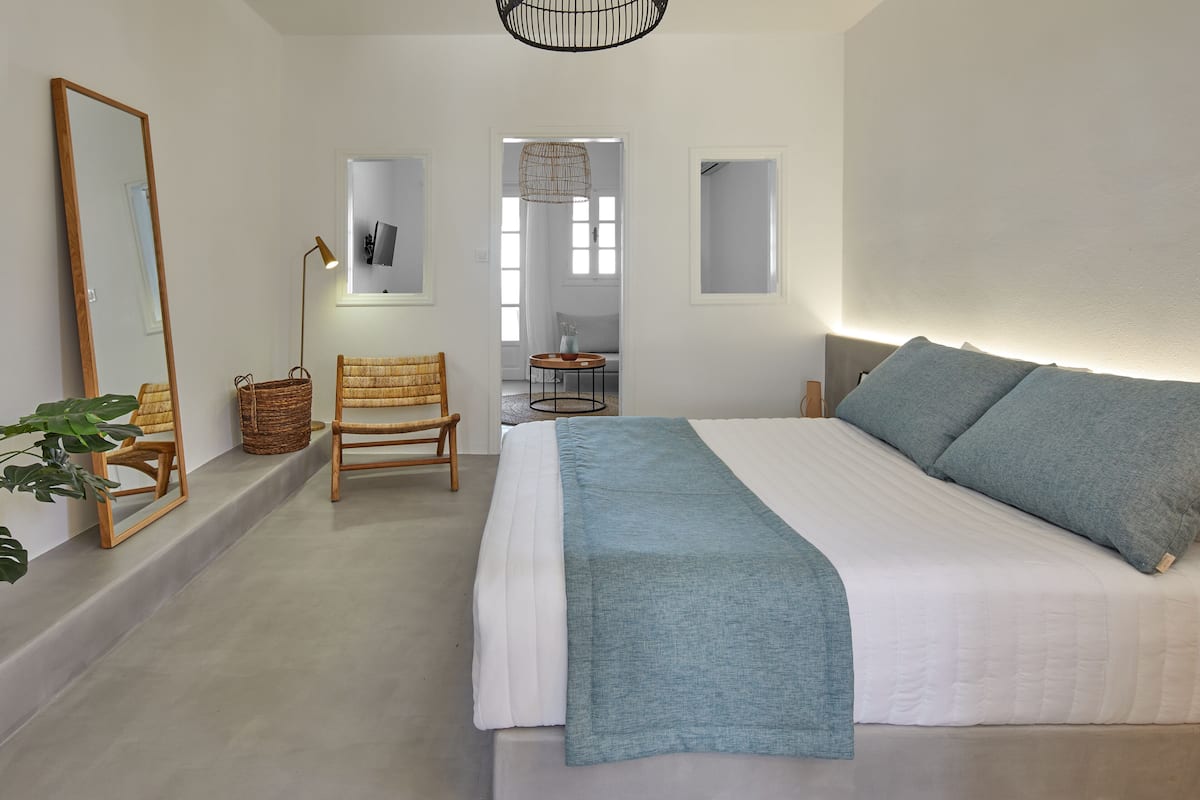 A bedroom with a bed, a chair, a mirror, and a small table.