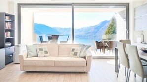 A modern living room with a large sliding glass door leading to a balcony with a mountain view. - In a panoramic position, modern apartment on the first floor of a new residence with SPA. Large windows frame the unique landscape of Lake COMO.This apartment has a beautiful terrace, with table and chairs and a sofa. The living room is a large open spac (Perledo)