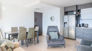 A modern living room with a dining area, a grey armchair, and a kitchen with a refrigerator and cabinets. - In a panoramic position, modern apartment on the first floor of a new residence with SPA. Large windows frame the unique landscape of Lake COMO.This apartment has a beautiful terrace, with table and chairs and a sofa. The living room is a large open spac (Perledo)